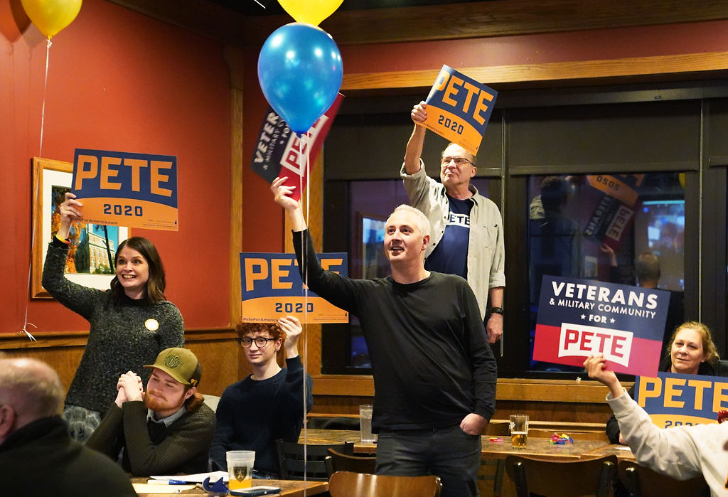 Supporters of Pete Buttigieg hold up campaign signs during their call with other remote watch parties for the candidate